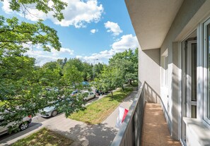 Un balcon donnant sur un parking et des arbres.