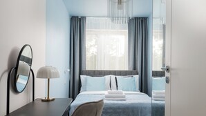 Ett hotellrum med en säng, ett skrivbord med en lampa, en spegel och utsikt över omgivningarna genom fönstret.