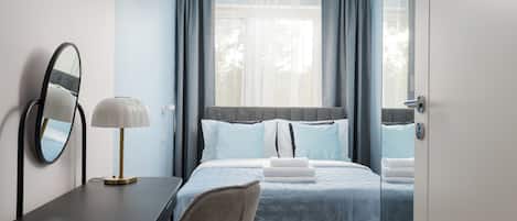 Habitación de hotel con cama, escritorio con lámpara, espejo y vista al exterior a través de la ventana.
