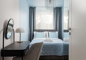 Habitación de hotel con cama, escritorio con lámpara, espejo y vista al exterior a través de la ventana.