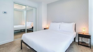 Ein Hotelzimmer mit einem großen Bett, einem Nachttisch mit Lampe, einem Spiegel und einer Schiebetür zu einem weiteren Raum.
