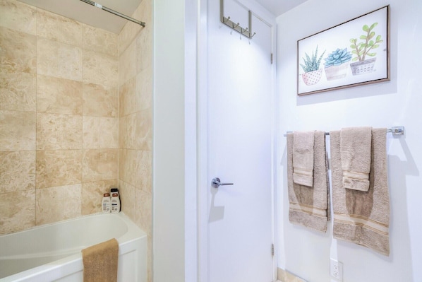 A bathroom with a bathtub, a shower, and a door with a towel rack. - Exclusive 1BR Hotel Suite at The Velaire Toronto (Toronto)