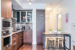 A modern kitchen with built-in appliances, a dining area with stools, and a visible door leading to another room. - Exclusive 1BR Hotel Suite at The Velaire Toronto (Toronto)