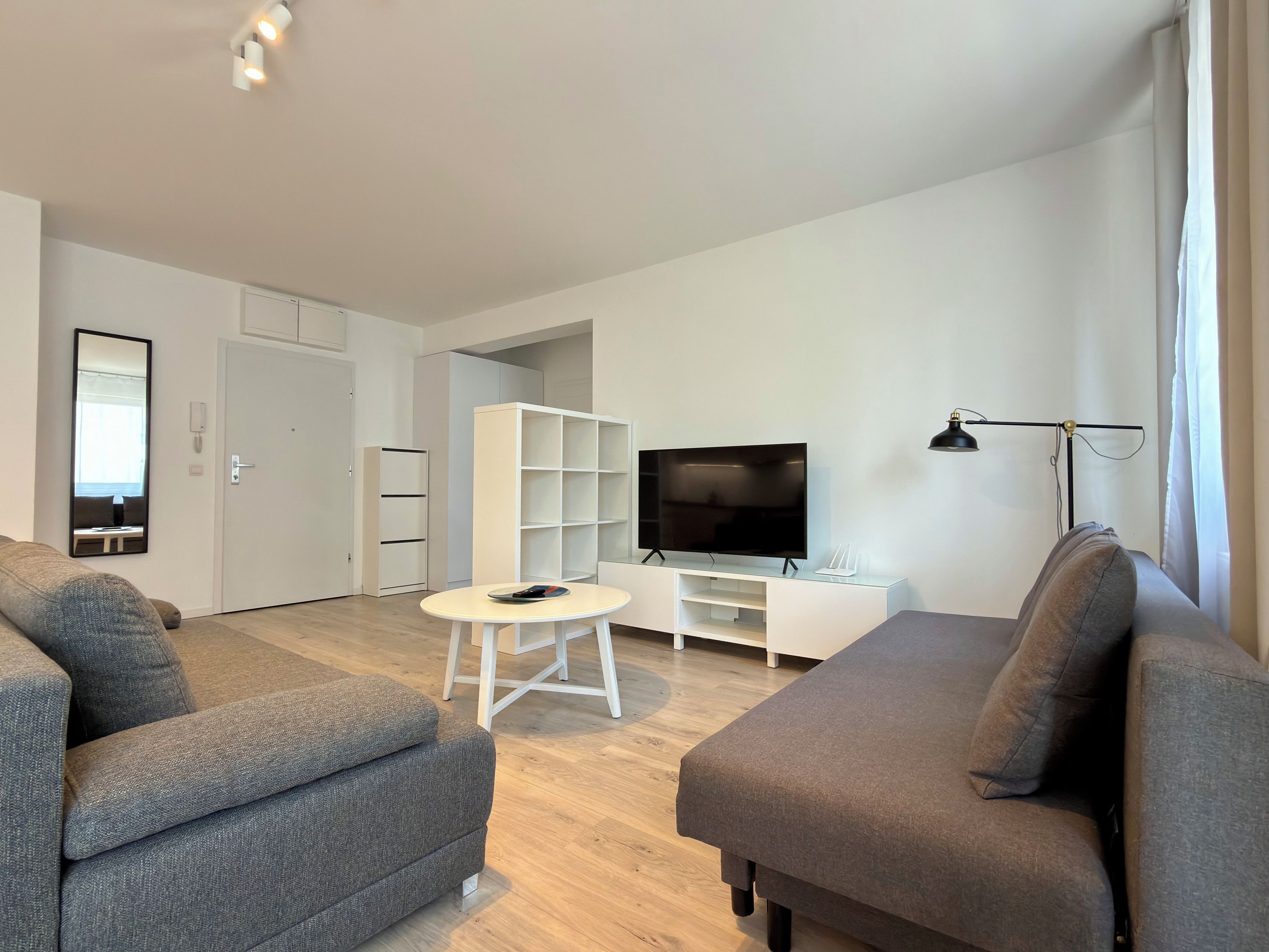 A modern living room with a sofa, a television, a white cabinet, and a small table.