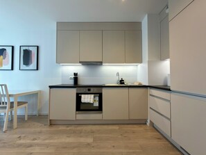 A modern kitchen with a built-in oven, a sink, and a dining area with a chair. - Mieszczańska Harmony Apartment (Wrocław)