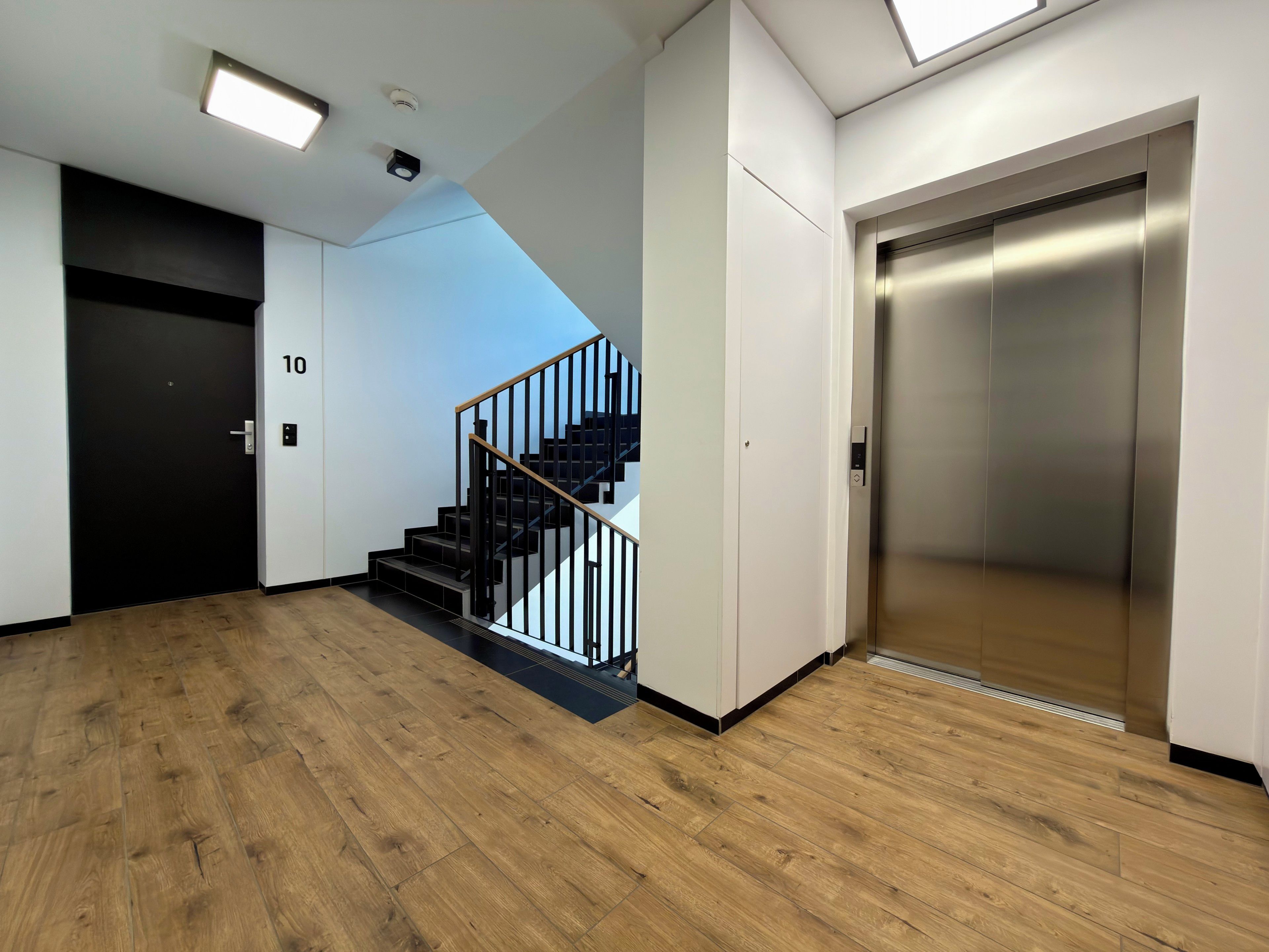 Ein modernes Interieur mit Holzboden, einer schwarzen Treppe und einem Aufzug.