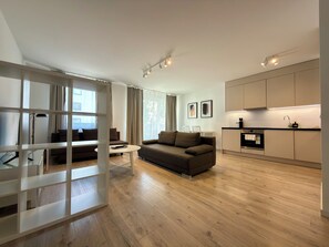 A modern living room with a sofa, a dining table, and a kitchen area with cabinets and a countertop. - Mieszczańska Harmony Apartment (Wrocław)