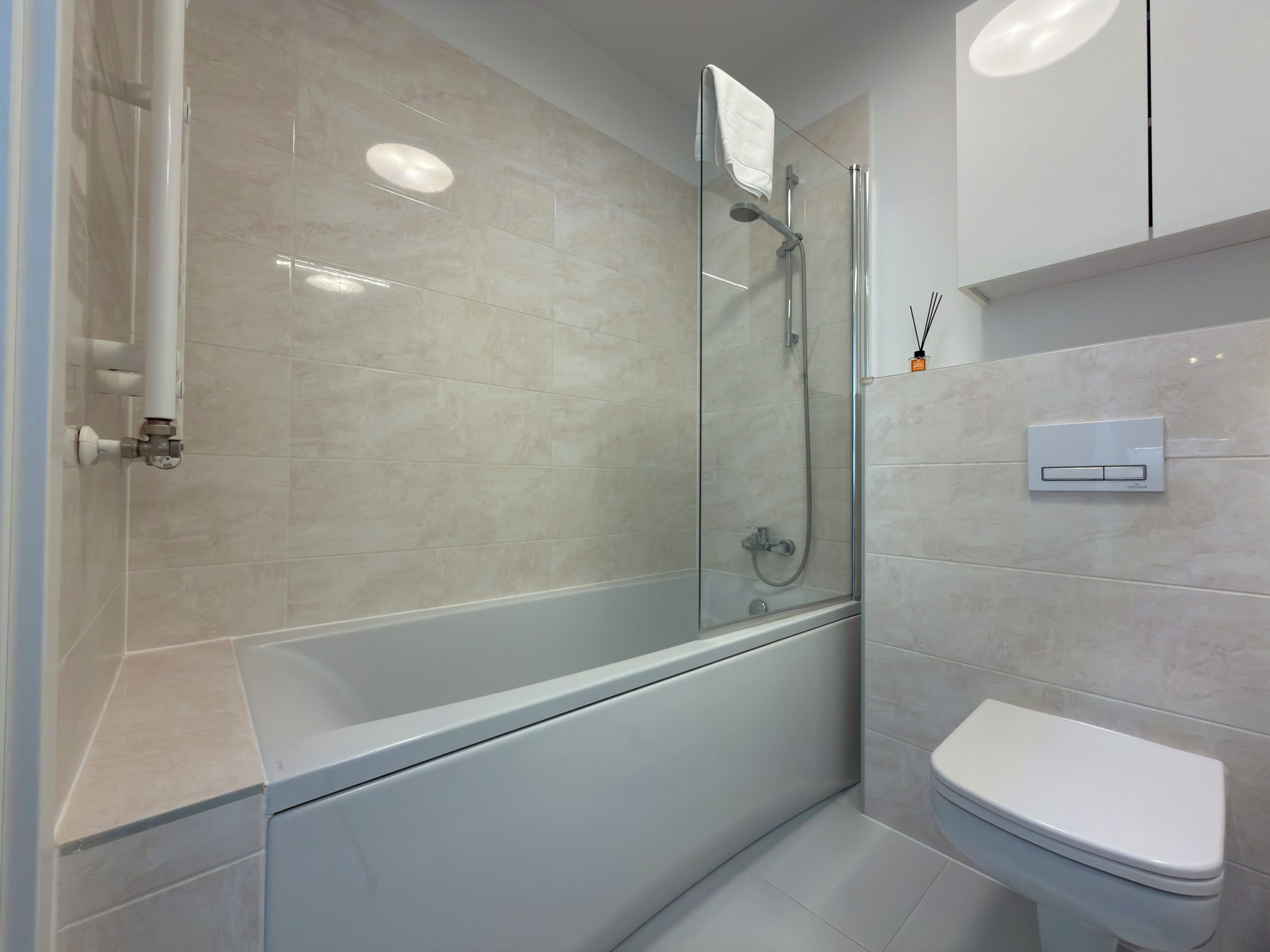 Un baño moderno con ducha envuelta en vidrio, inodoro blanco y panel de control en la pared.