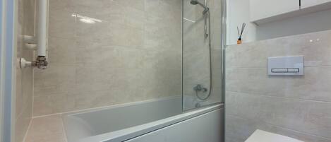 Un baño moderno con ducha envuelta en vidrio, inodoro blanco y panel de control en la pared.