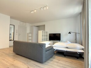 A modern bedroom with a grey sofa, a bed with white bedding, a TV, and a bedside table. - Mieszczańska Harmony Apartment (Wrocław)