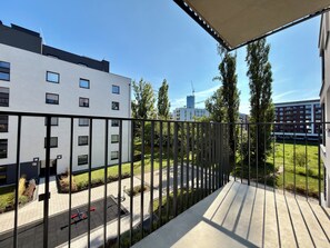 A balcony with a view of a modern building, a parking area, and a grassy landscape. - Mieszczańska Harmony Apartment (Wrocław)