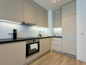 A modern kitchen with a built-in oven, a stainless steel range hood, and a black countertop. - Mieszczańska Harmony Apartment (Wrocław)