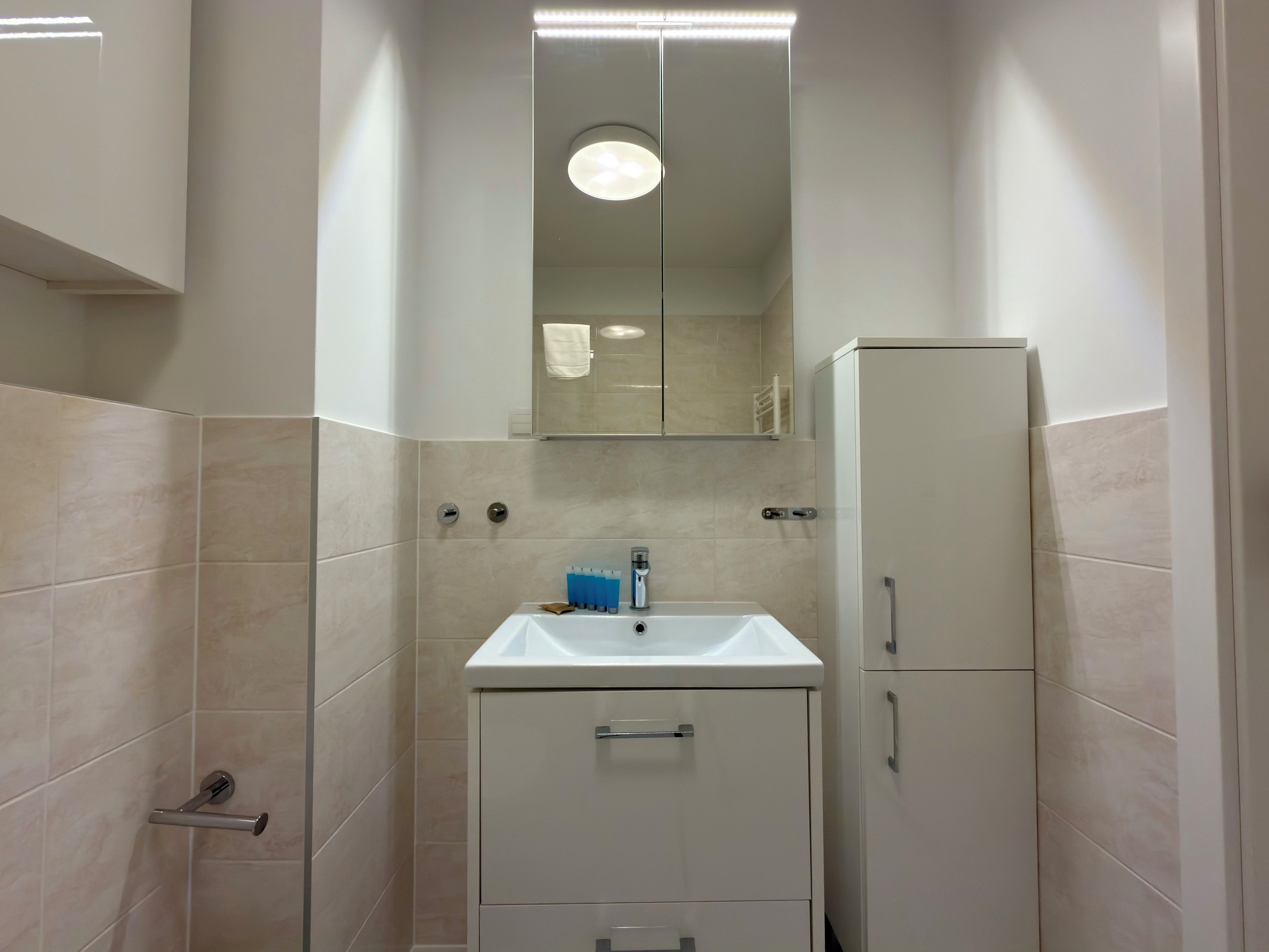 A bathroom with a white sink, mirror, and cabinets.