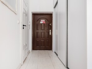 A hallway with a wooden door, white walls, and a white floor. - Park Źródliska White & Brick Studio (Łódź)