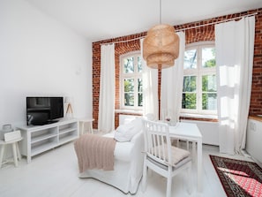 Een lichte kamer met een televisie, witte meubels en een bakstenen muur.