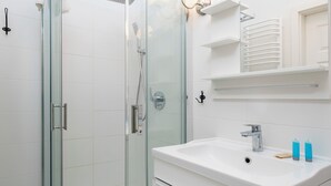 Ett modernt badrum med en dusch som är avskärmad med glasväggar, ett vitt handfat och en spegel ovanför.