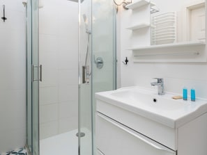 Een moderne badkamer met een douchecabine van glas, een witte wastafel en een spiegel erboven.