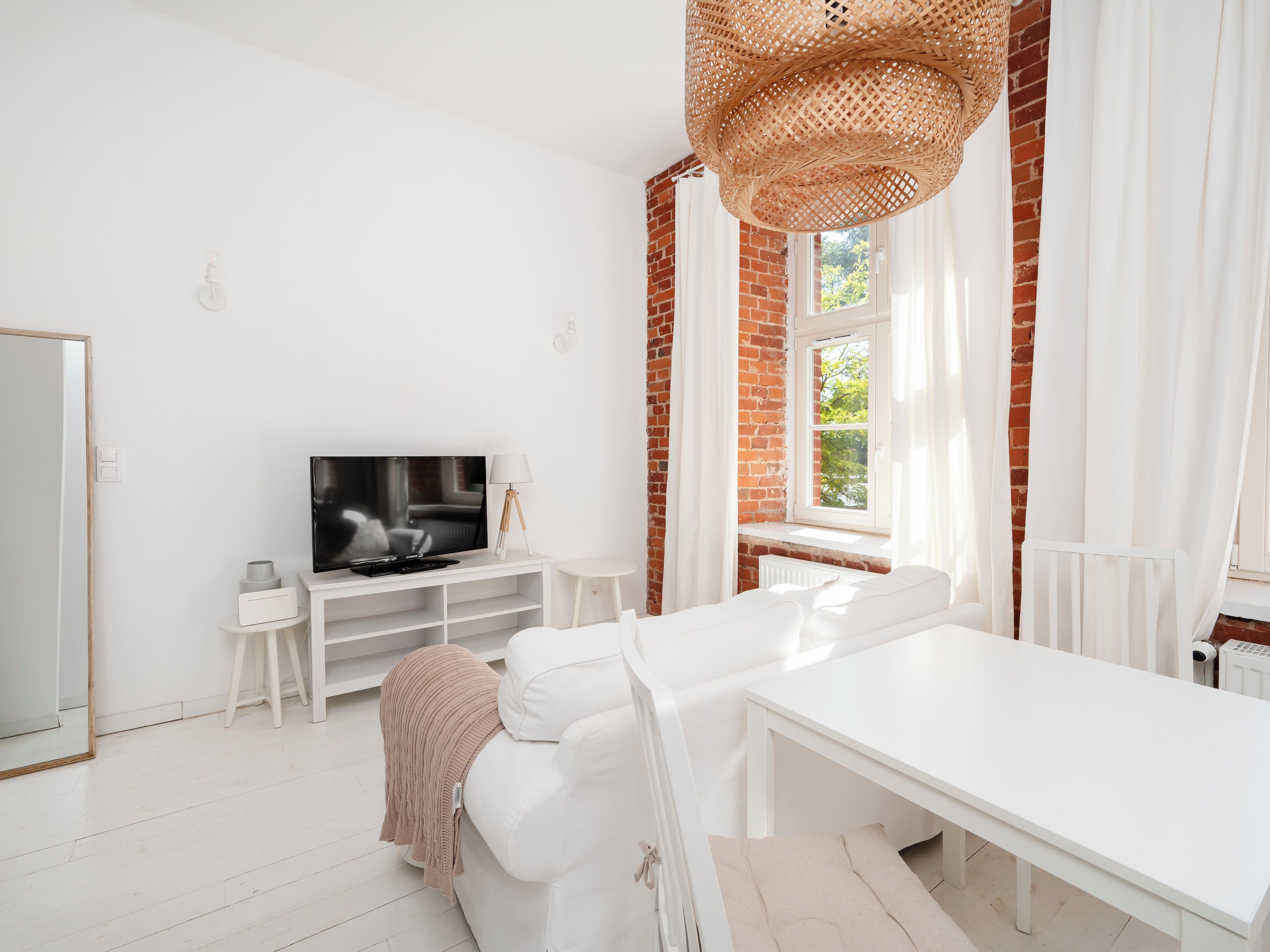 A modern living room with a white sofa, a TV on a stand, a white table, and a large woven light fixture.