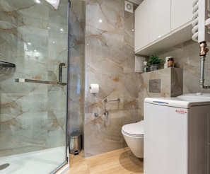 A modern bathroom with a glass shower enclosure, a toilet, and a white washing machine. - Sopot Peaceful Retreat Apartment (Sopot)