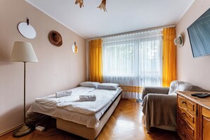 Una habitación de hotel con cama, escritorio, silla, lámpara y ventana con cortinas.