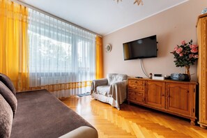 Ein Wohnzimmer mit einer Couch, einem an der Wand befestigten Fernseher und einem Schrank mit einem Blumenstrauß.