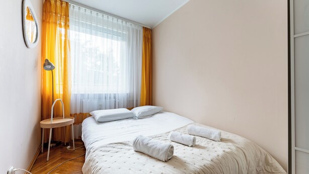 Ein Schlafzimmer mit einem Bett, einem Nachttisch, einer Lampe und einem Fenster mit Vorhängen.