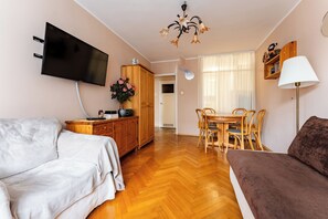 A living room with a flat-screen TV, wooden furniture, a dining table with chairs, a sofa, and a lamp. - Sopot Peaceful Retreat Apartment (Sopot)