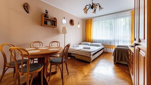 Ein gemütliches Zimmer mit einem Holzesstisch, Stühlen, einem Bett, einer Couch und einem Fenster mit Vorhängen.