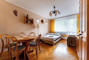 A cozy room with a wooden dining table, chairs, a bed, a sofa, and a window with curtains. - Sopot Peaceful Retreat Apartment (Sopot)