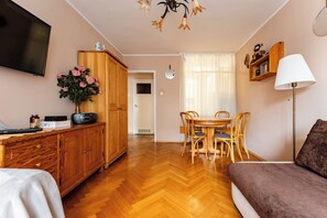 A living room with a wooden floor, a TV mounted on the wall, a dining area with a table and chairs, and a sofa. - Sopot Peaceful Retreat Apartment (Sopot)