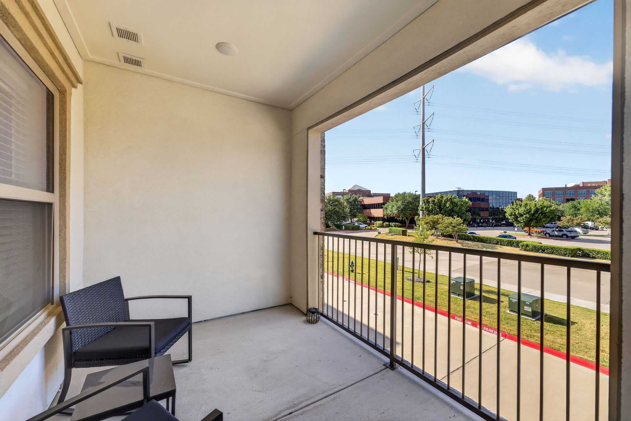 Un balcon avec une chaise, une vue sur un parking et des bâtiments en arrière-plan.