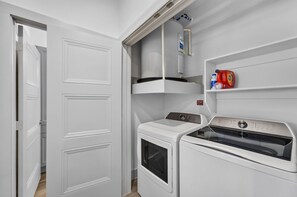 Ett litet och praktiskt tvättrum med tvättmaskin, torktumlare och en hylla med flaskor innehållande tvättmedel.