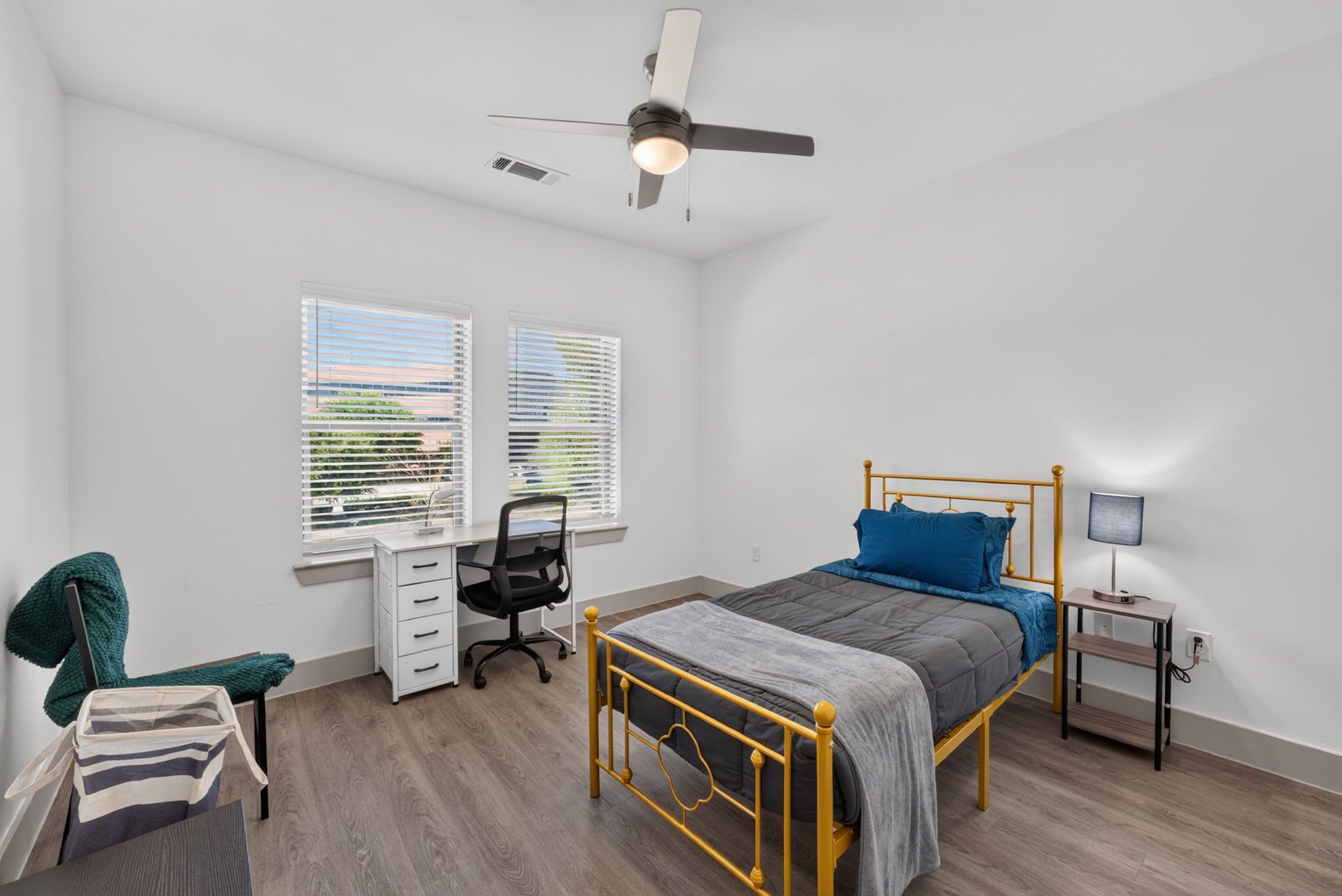 A bedroom with a bed, desk, chair, and a ceiling fan.