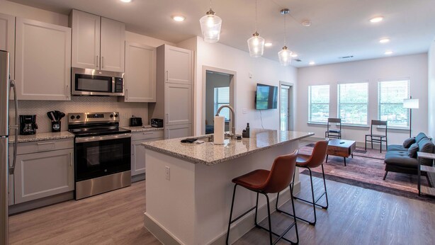 Una cocina moderna con electrodomésticos de acero inoxidable, una isla central con taburetes y un comedor con sofá y sillas.