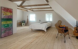 A bedroom with a sloped ceiling, a bed, a chair, a guitar, and a painting. - Nice home in Tranekær with WiFi (Tranekær)