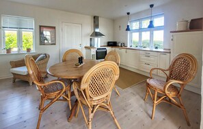 A kitchen with a round dining table surrounded by wicker chairs, a built-in oven, and a window with blinds. - Nice home in Tranekær with WiFi (Tranekær)