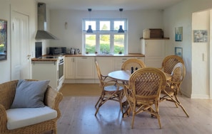 A compact kitchen with white cabinets, a dining table with wicker chairs, and a window overlooking greenery. - Nice home in Tranekær with WiFi (Tranekær)