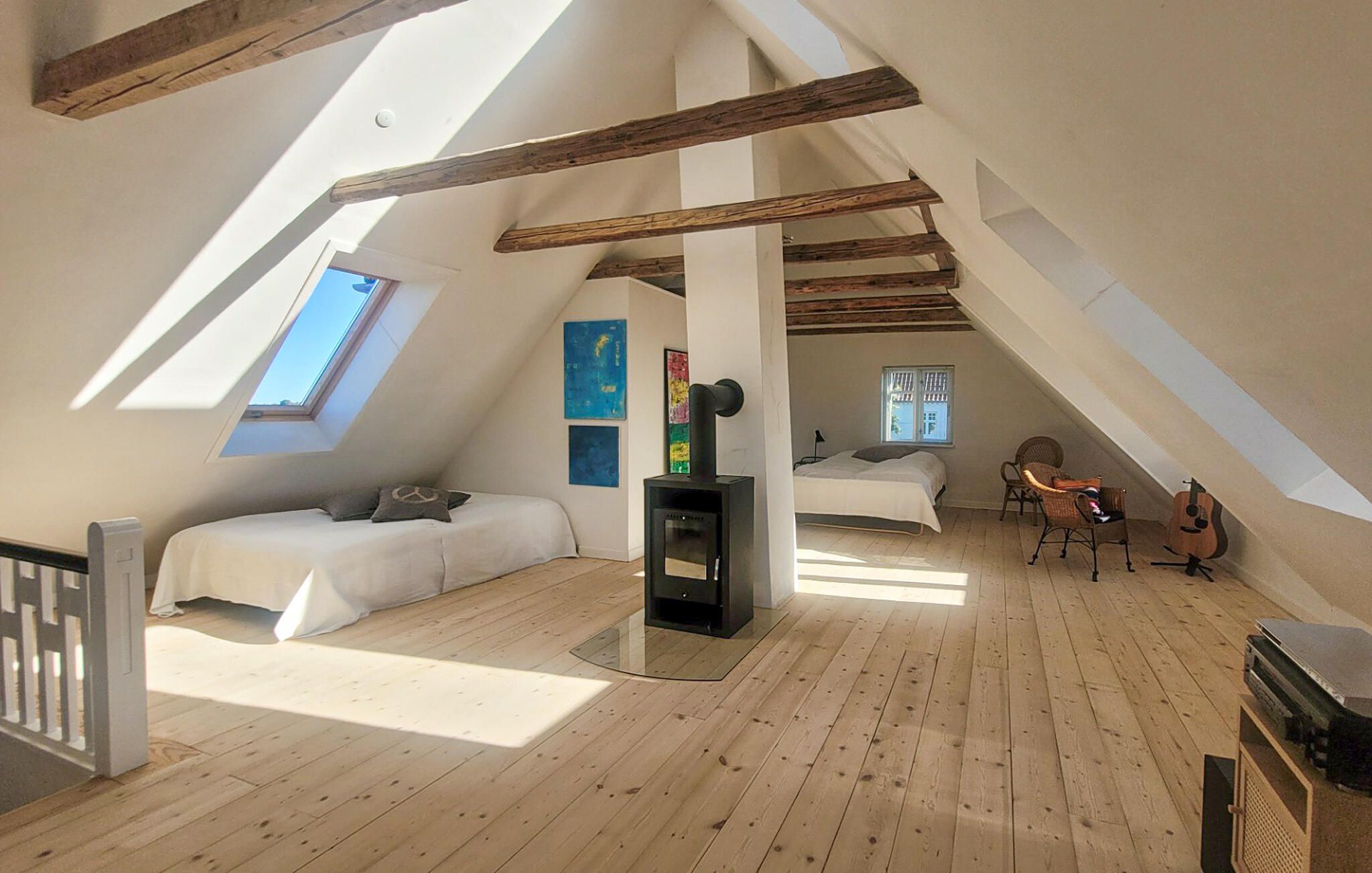 Camera mansardata con tetto spiovente, travi in legno, un letto, un tavolino, una sedia e un camino.
