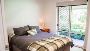 A bedroom with a bed, a nightstand, a lamp, and a view through a window. - Hop, Skip and a Jump - Entire vacation home on acreage (Landsborough)