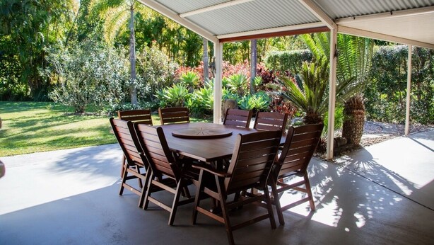 An outdoor patio with a round table and chairs, surrounded by lush greenery and a covered area. - Hop, Skip and a Jump - Entire vacation home on acreage (Landsborough)