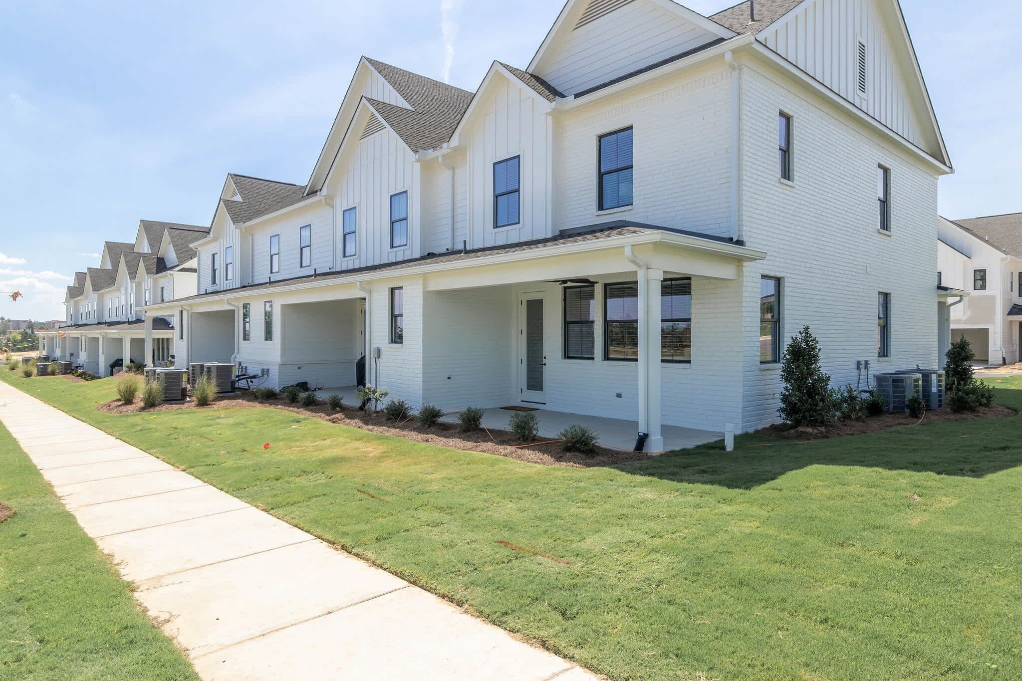A row of modern townhouses with a covered front porch, a well-maintained lawn, and a clear sky.