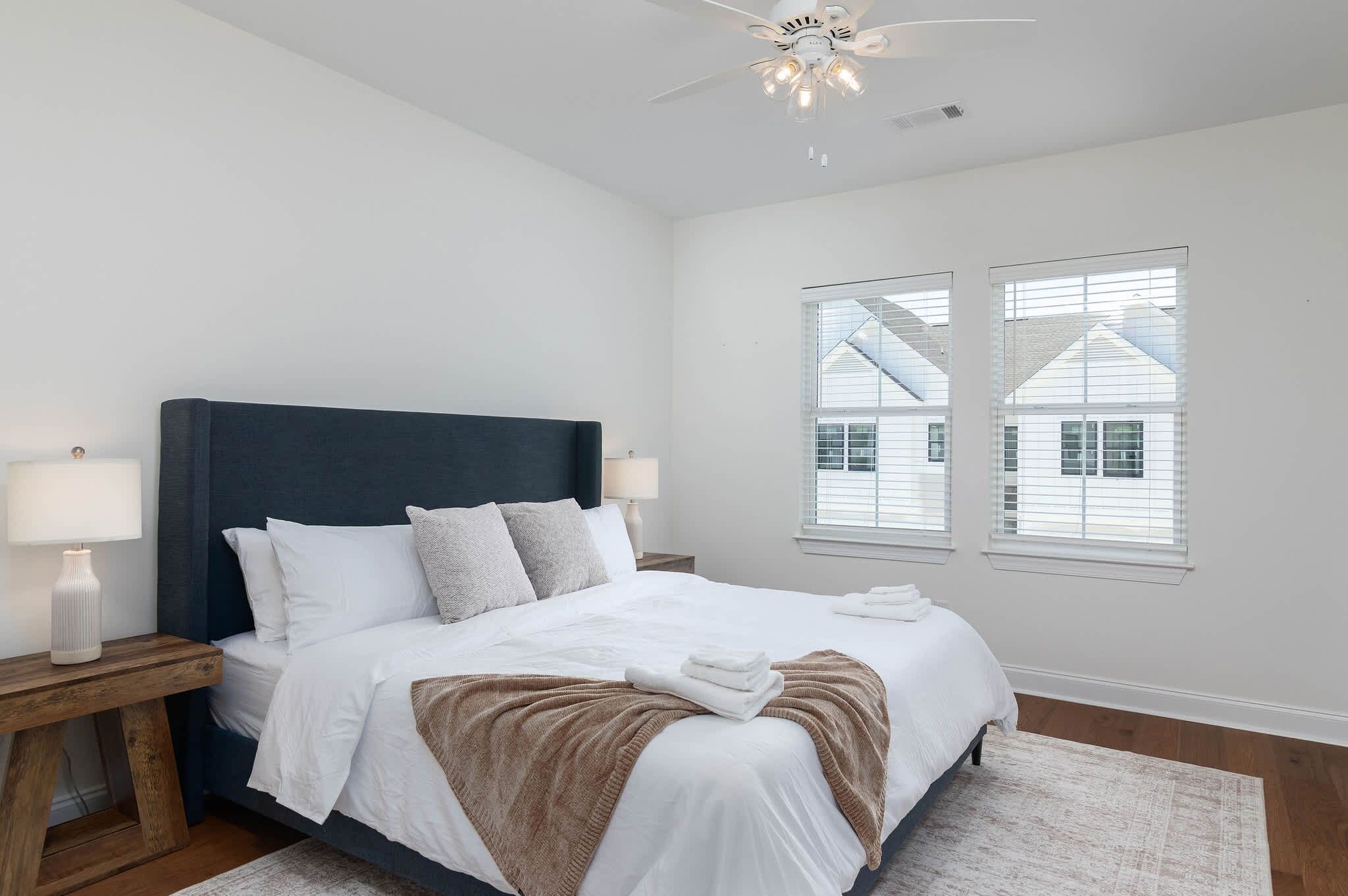 A bedroom with a bed, two bedside tables, a ceiling fan, and a window with blinds.