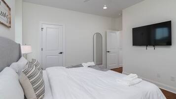 A modern bedroom with a bed, a flat-screen TV, a ceiling fan, and a mirror.