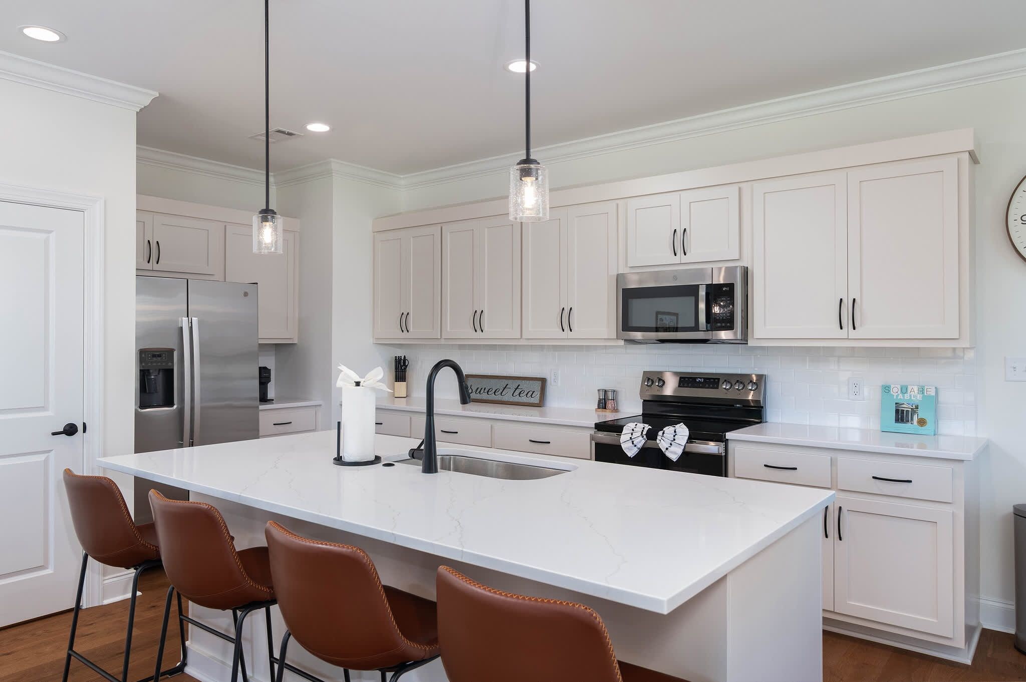 A modern kitchen with white cabinetry, a central island with bar stools, stainless steel appliances, and pendant lighting.