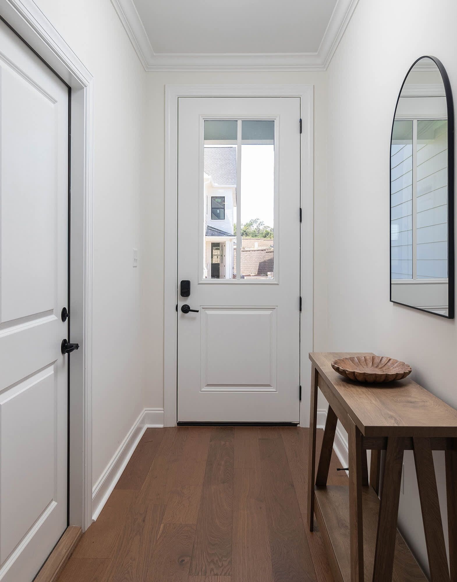 A hallway with a white door, a small table with a bowl, and a mirror on the wall.