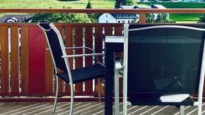 A balcony with a table and chairs, overlooking a green landscape with buildings in the distance. - Haus Alpina (CharmingStay). 2.5-Zimmerwohnung mit zwei Balkonen by Interhome (Mols)