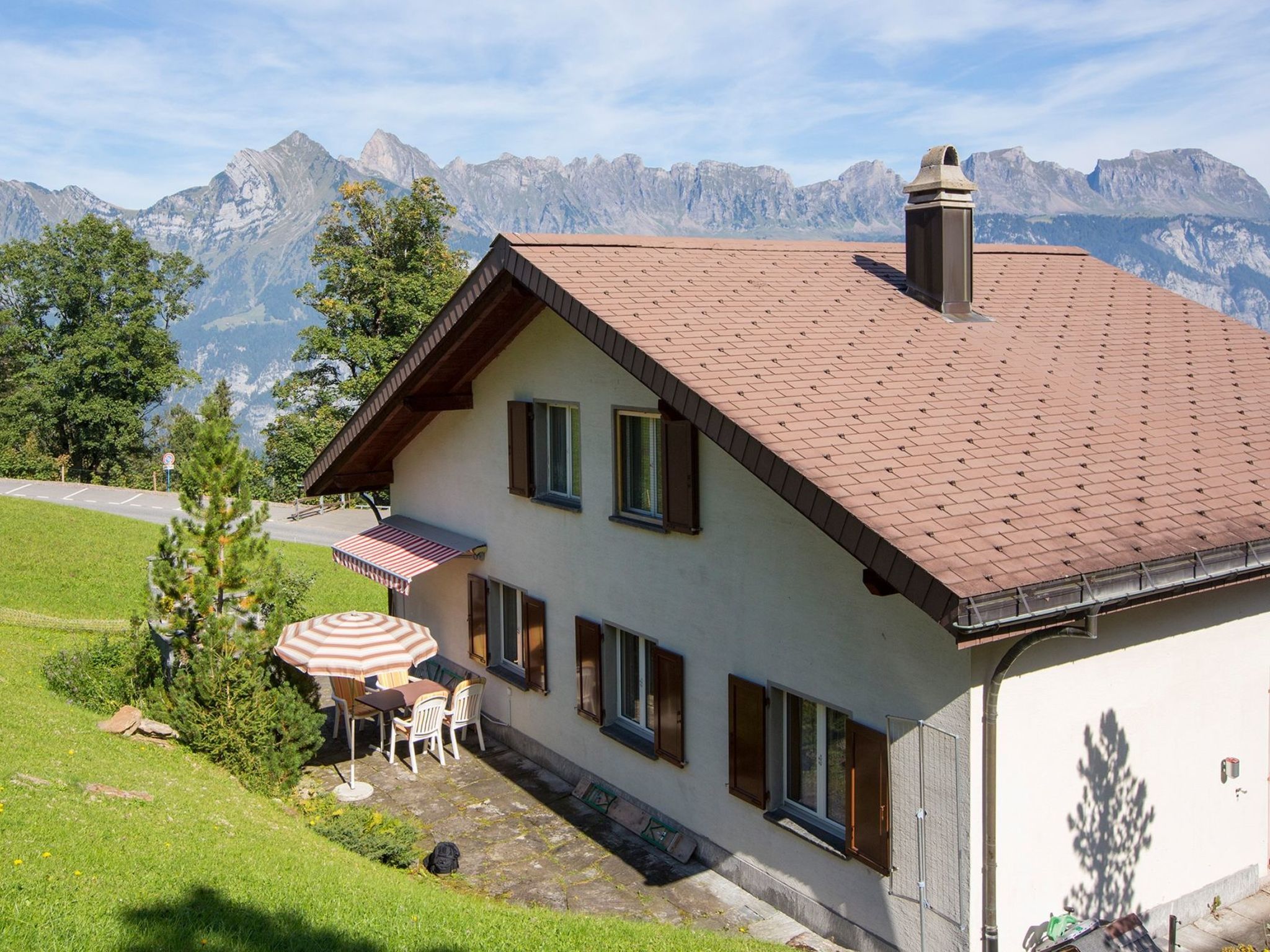 Una casa con techo inclinado, chimenea y un patio con sombrilla.