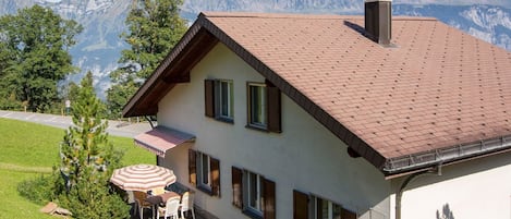 Une maison avec un toit en pente, une cheminée et une terrasse dotée d’un parasol.