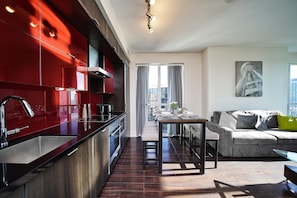 A modern kitchen with a red backsplash, a dining area with a bench, and a living room with a sofa and a painting on the wall. - Modern 2 Bedroom Suite Downtown Stay - Near CN Tower & Rogers Centre (Toronto)