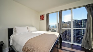 Ein Hotelzimmer mit einem großen Bett und Blick auf die Stadt durch raumhohe Fenster, mit Stadtansicht im Hintergrund.